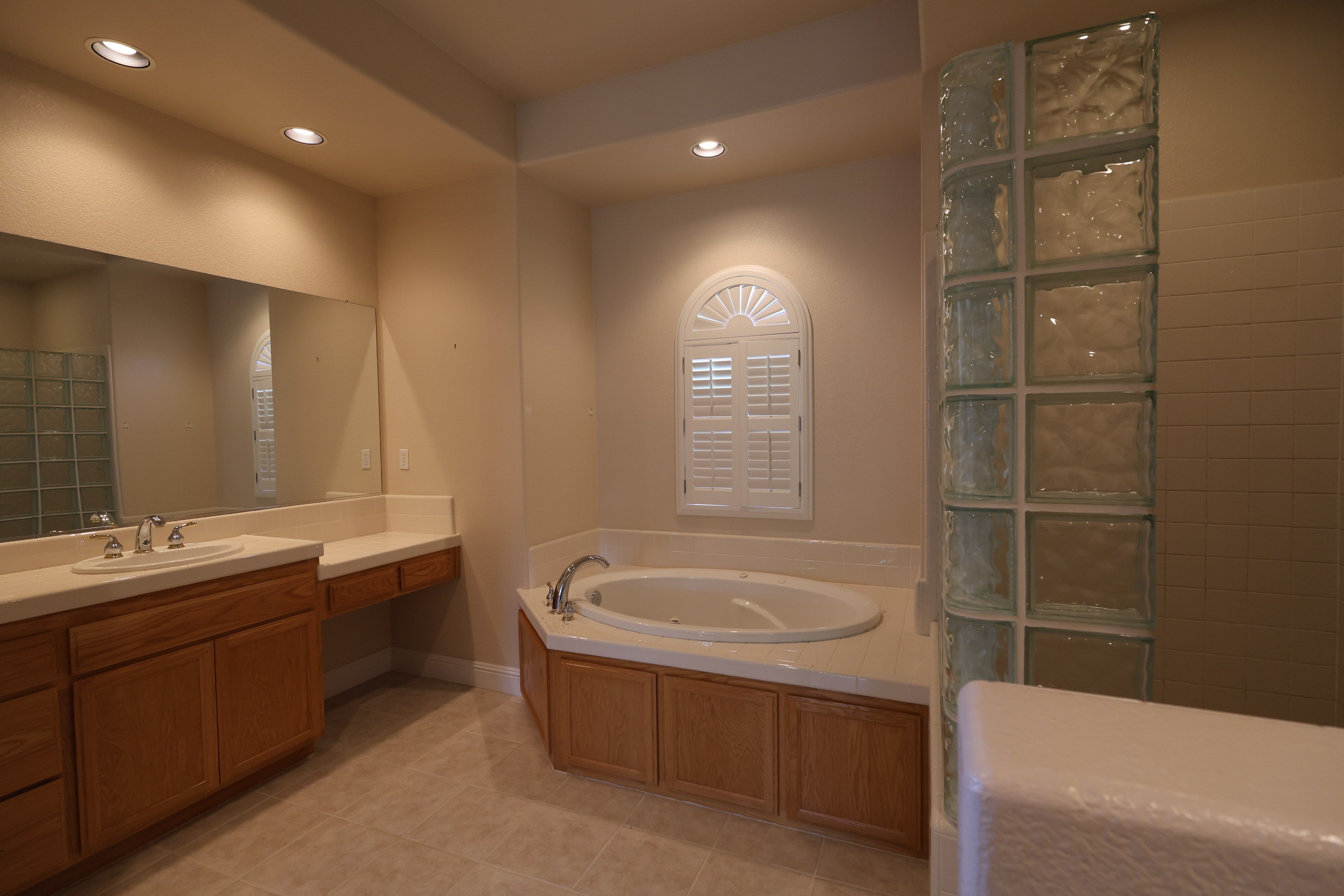 Dated master bathroom with oak vanity, glass block wall and drop-in jetted tub before remodeling