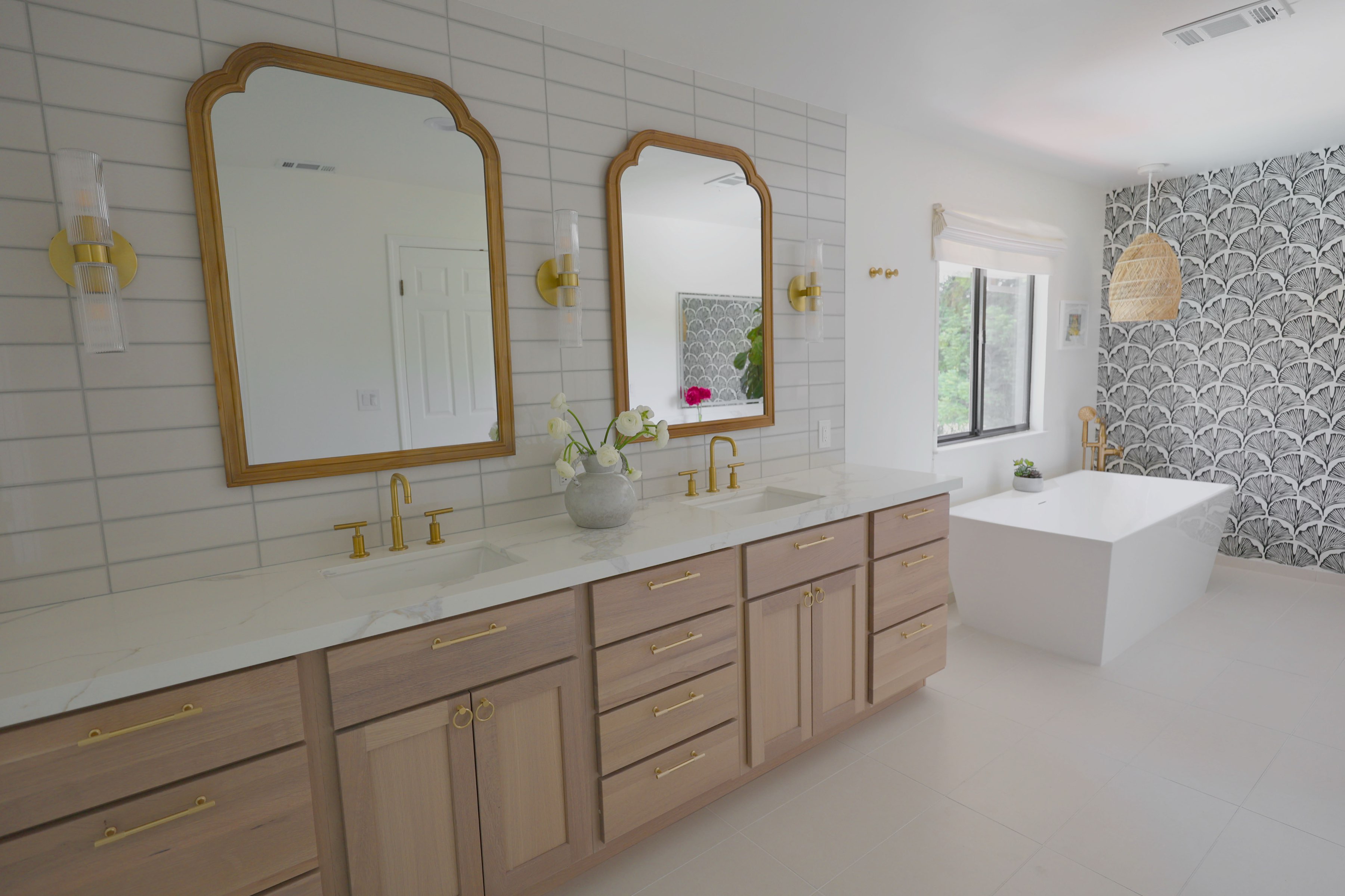 Bright remodeled bath with white oak double vanity, brass fixtures and freestanding tub