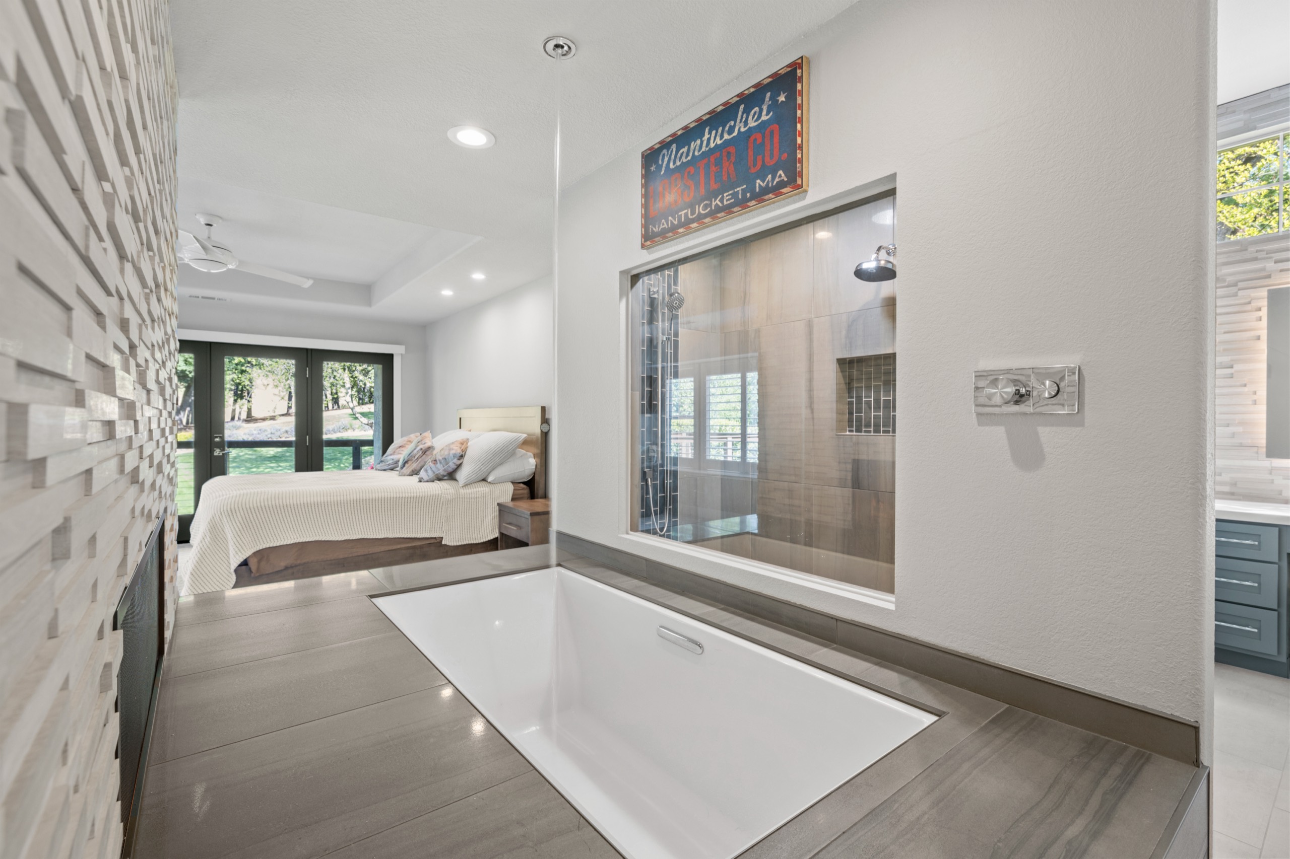 Drop-in soaking tub with a glass window into the tiled shower, open to the bedroom after remodeling