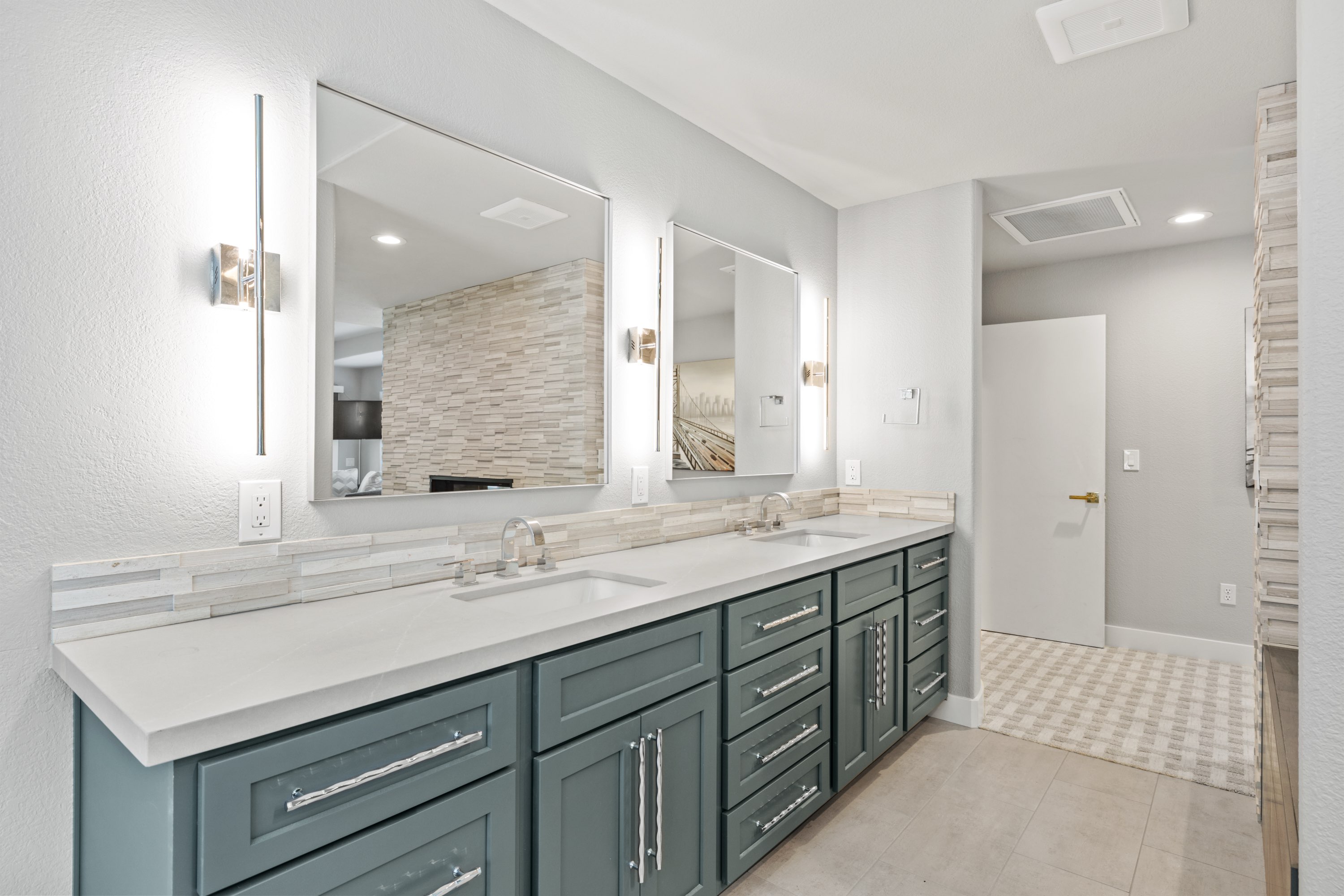 Deep green double vanity with quartz counters, stone backsplash and chrome sconces