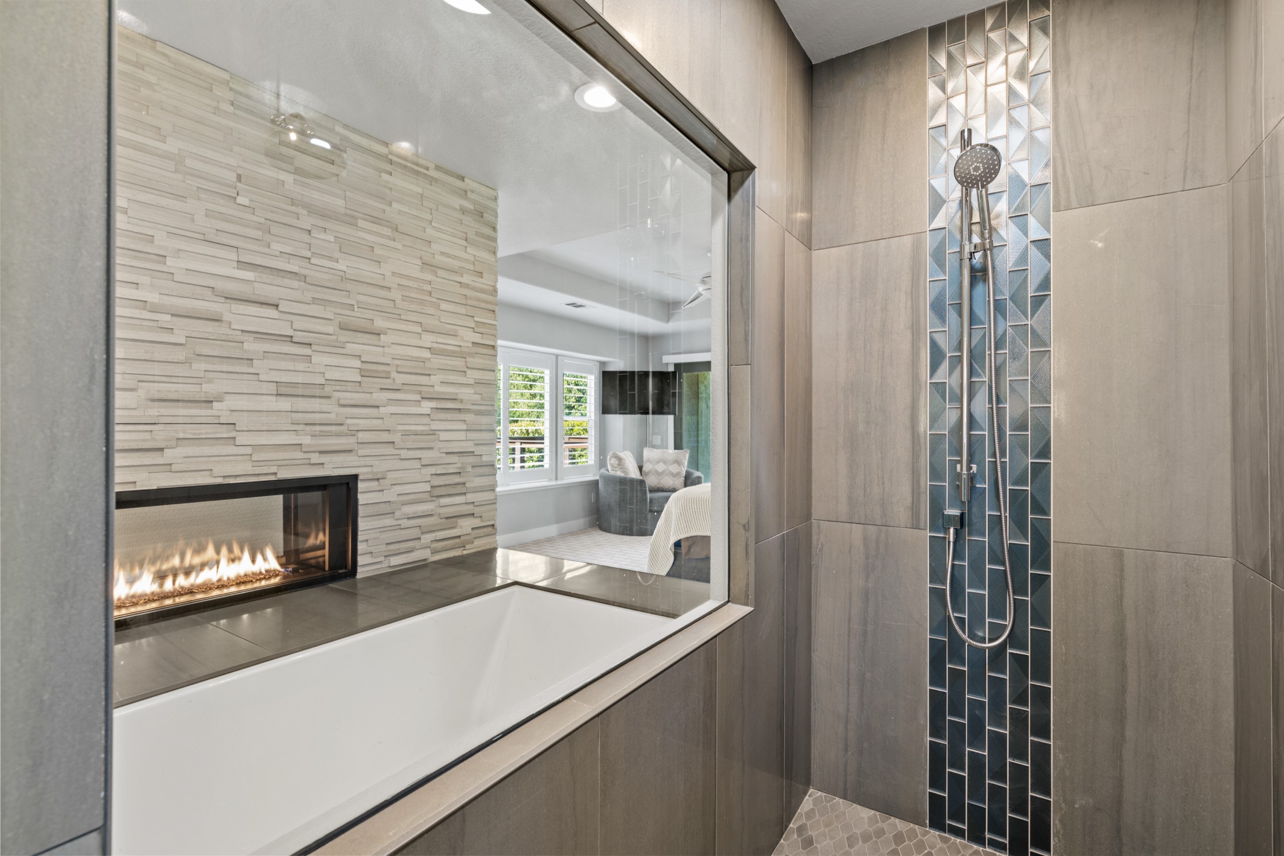 Tiled shower with mosaic accent column looking through to the fireplace and tub