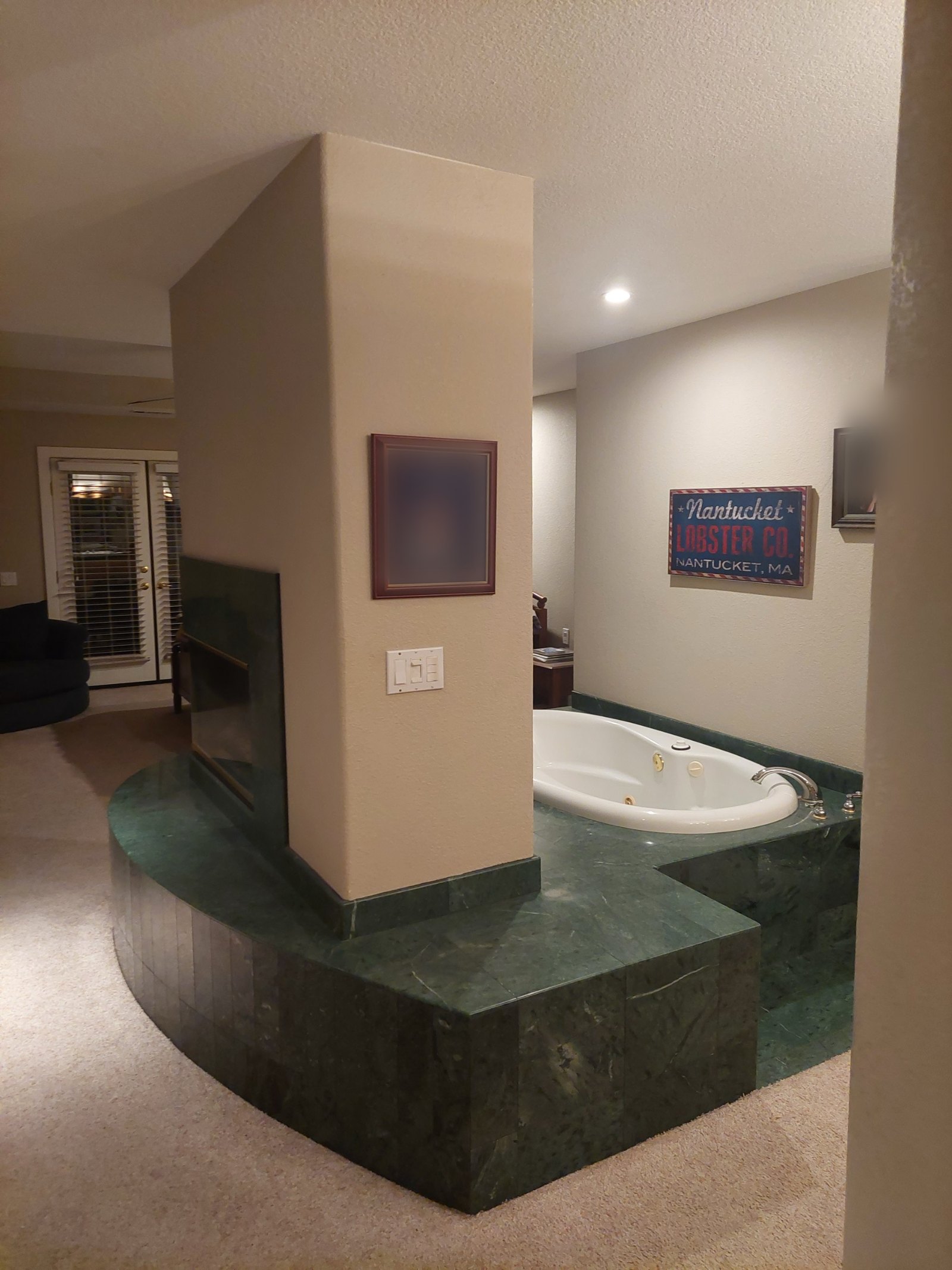 Original jetted tub set into a green marble platform with a see-through fireplace and carpet